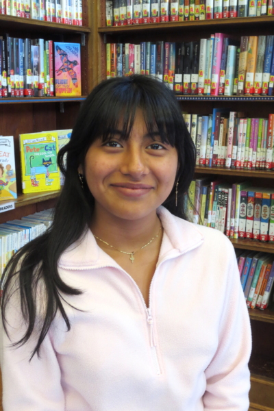A photo of Gisell Rodriguez Hernandez, Library Assistant, with library bookshelves in the background.