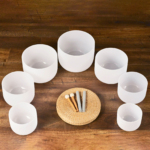 Crystal meditation bowls set in a semi-circle. Two pair of mallets rest on a round woven grass mat.